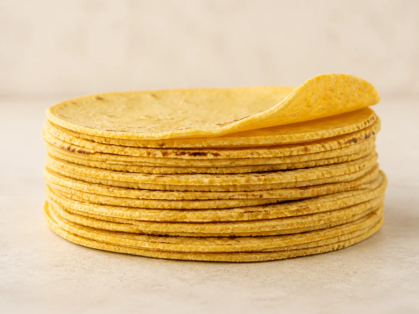 A tall stack of fresh yellow corn tortillas, the top one folded back
